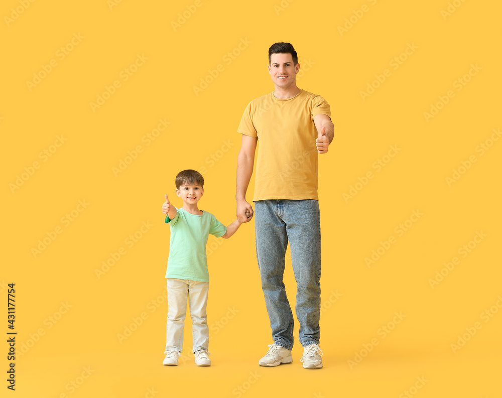 Happy father and his little son showing thumb-up on color background