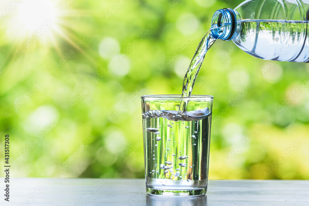 hand pouring water in bottle in to glass with sunshine on blur green backgound