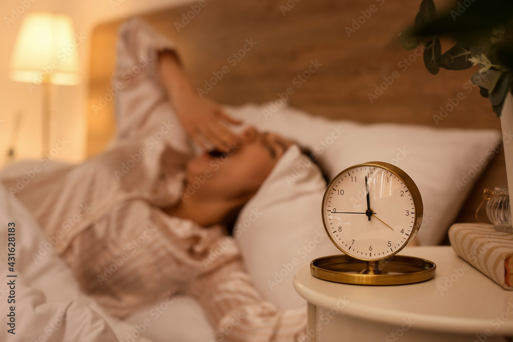 Alarm clock on table of sleepy young woman in bedroom