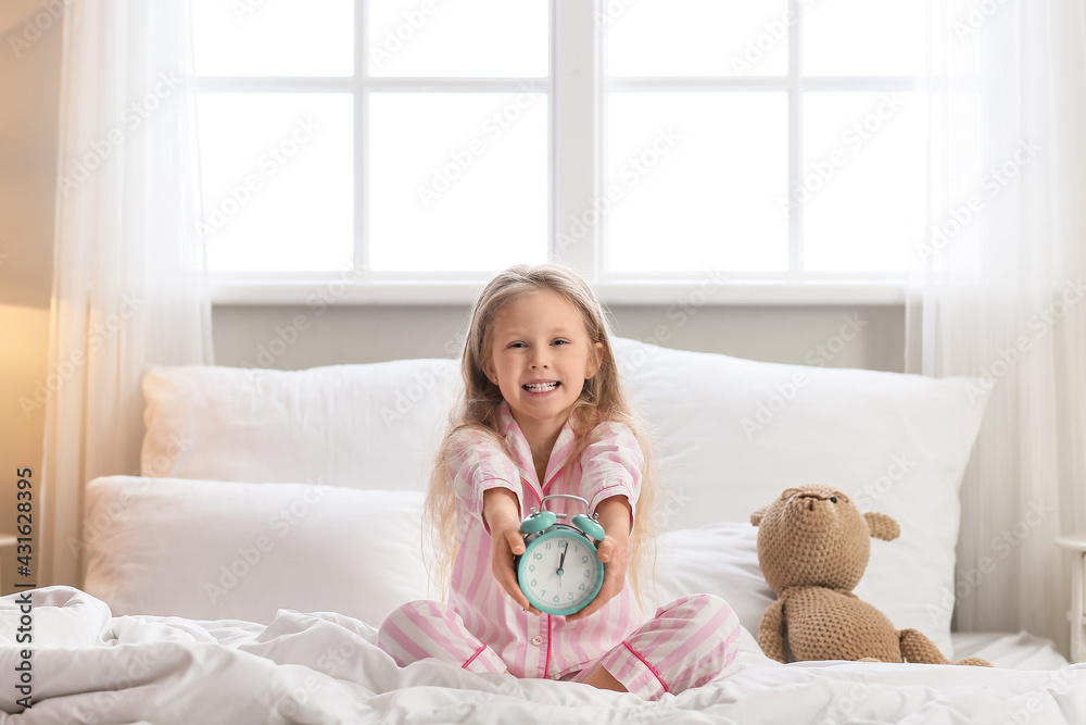 Cute little girl with alarm clock in bedroom