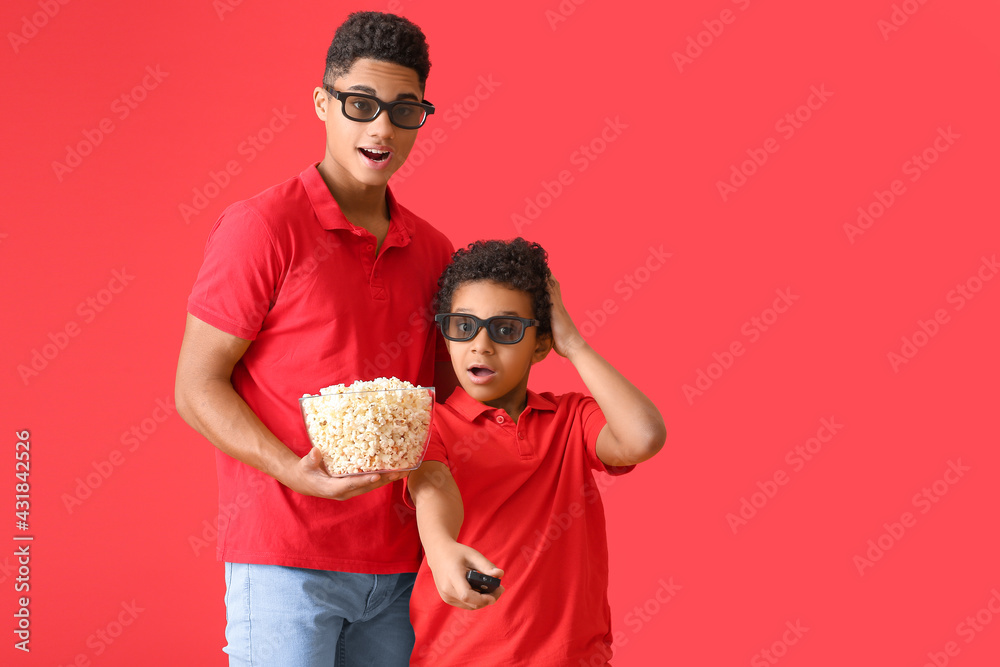 Shocked African-American boys watching movie on color background