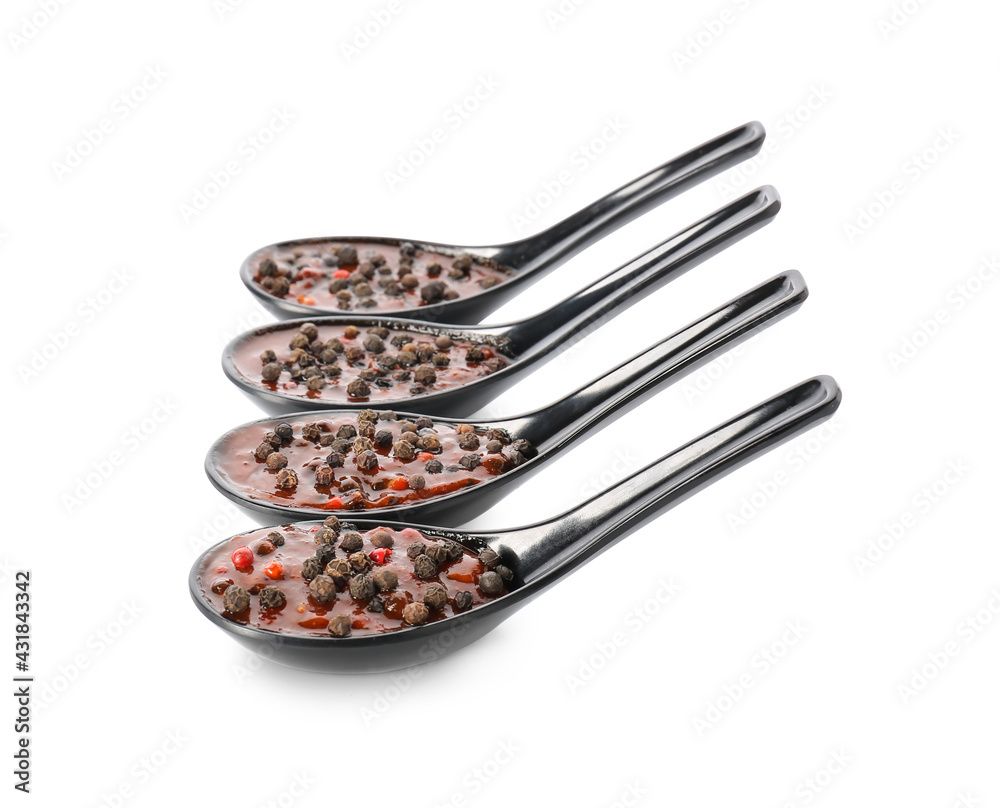 Spoons with peppercorn sauce on white background