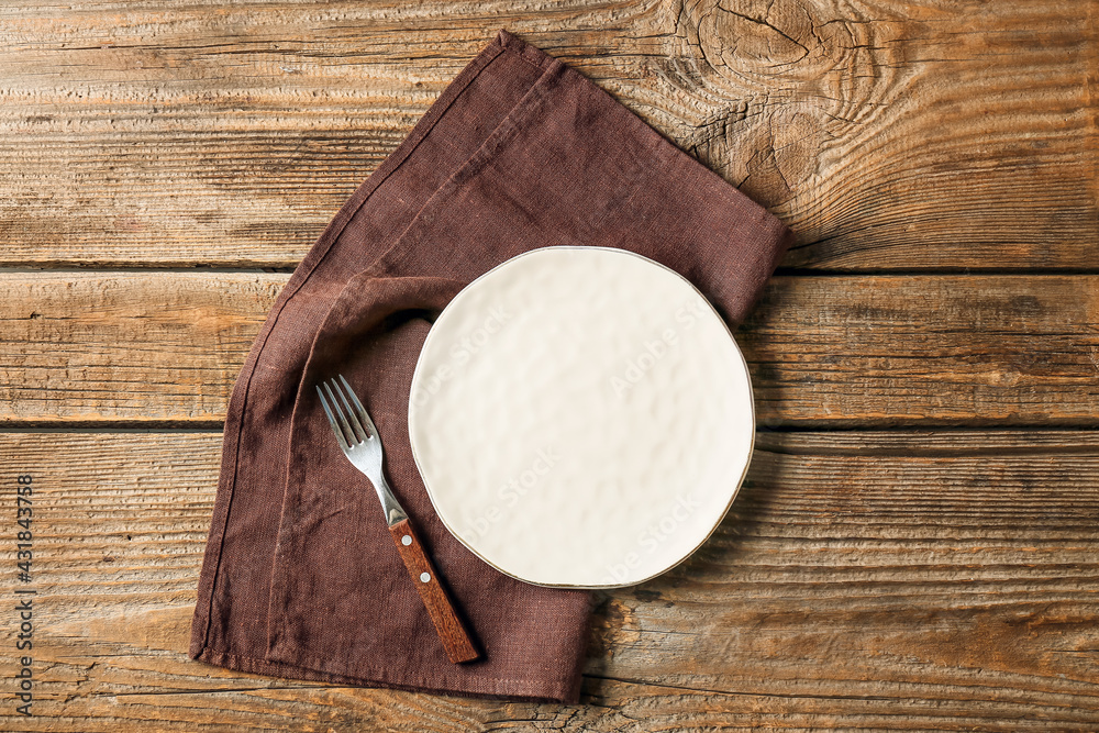 Plate, fork and stylish napkin on wooden background