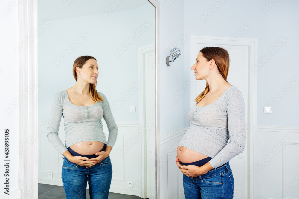 Late stage pregnancy woman posing near mirror