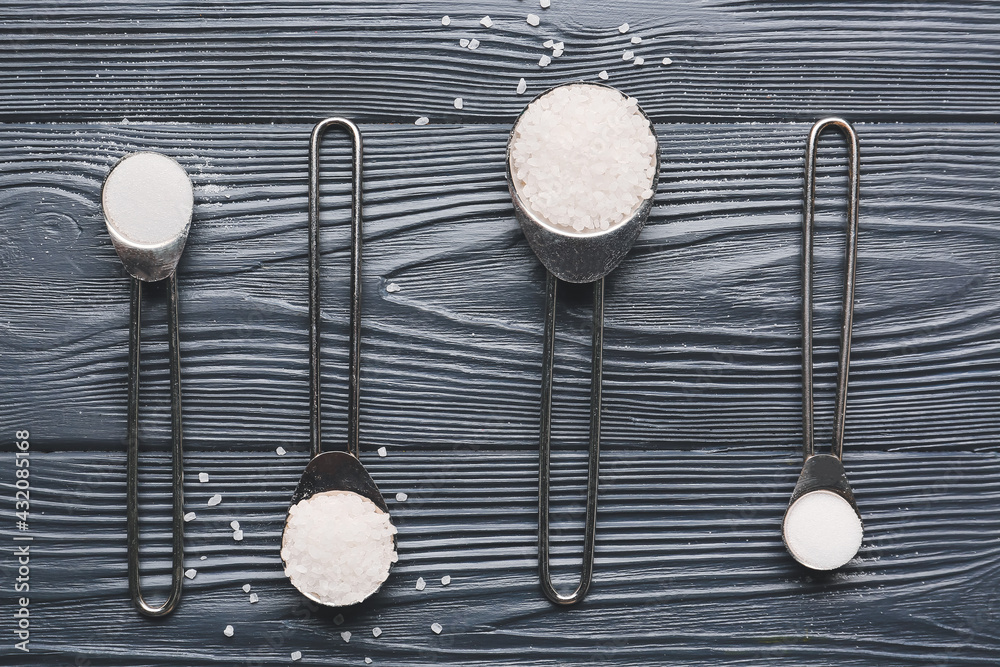 Spoons with salt on dark wooden background