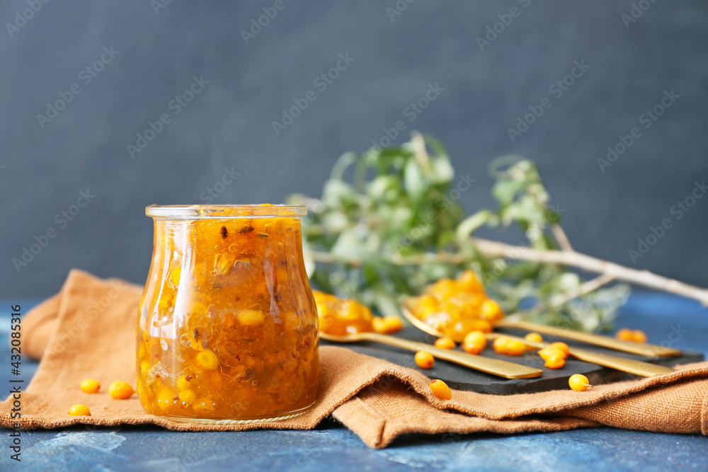 Jar of healthy sea buckthorn jam on color background