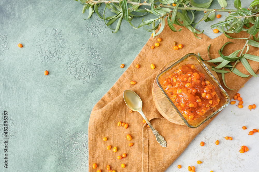 Bowl of healthy sea buckthorn jam on color background