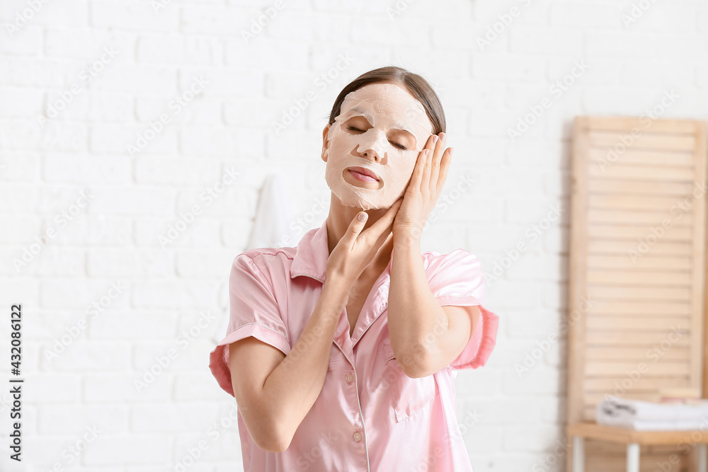 Beautiful young woman with sheet facial mask in bathroom