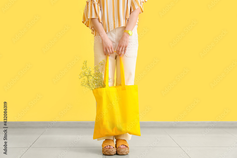 Stylish young woman with shopping bag near yellow wall