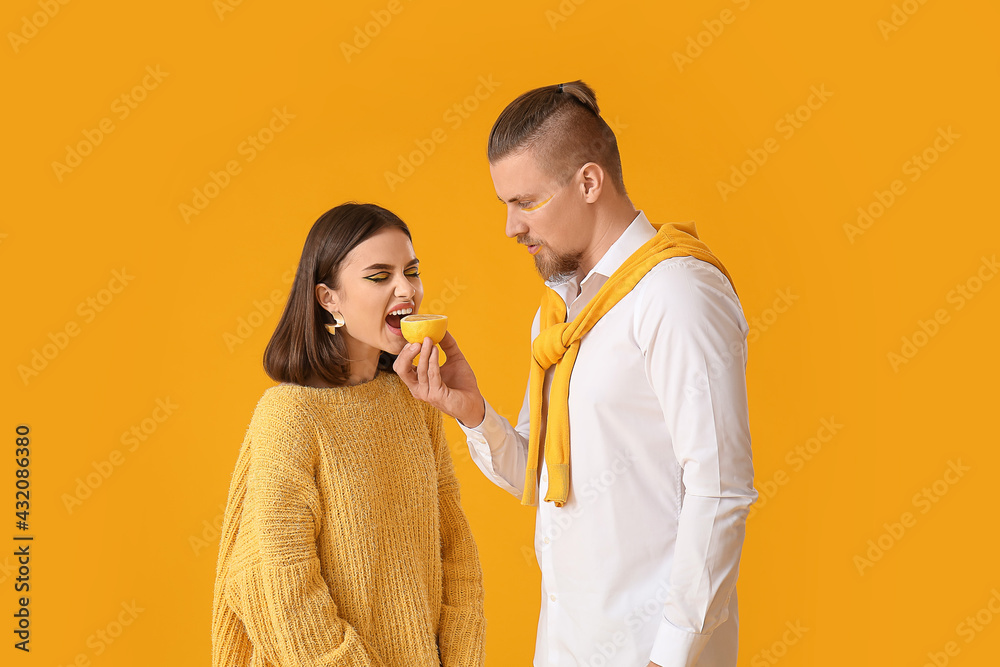 Stylish young couple with lemon on yellow background