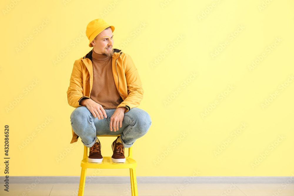 Stylish young man sitting on chair near yellow wall