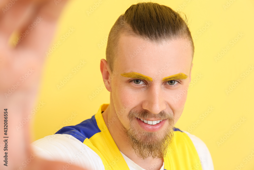 Stylish young man taking selfie on yellow background