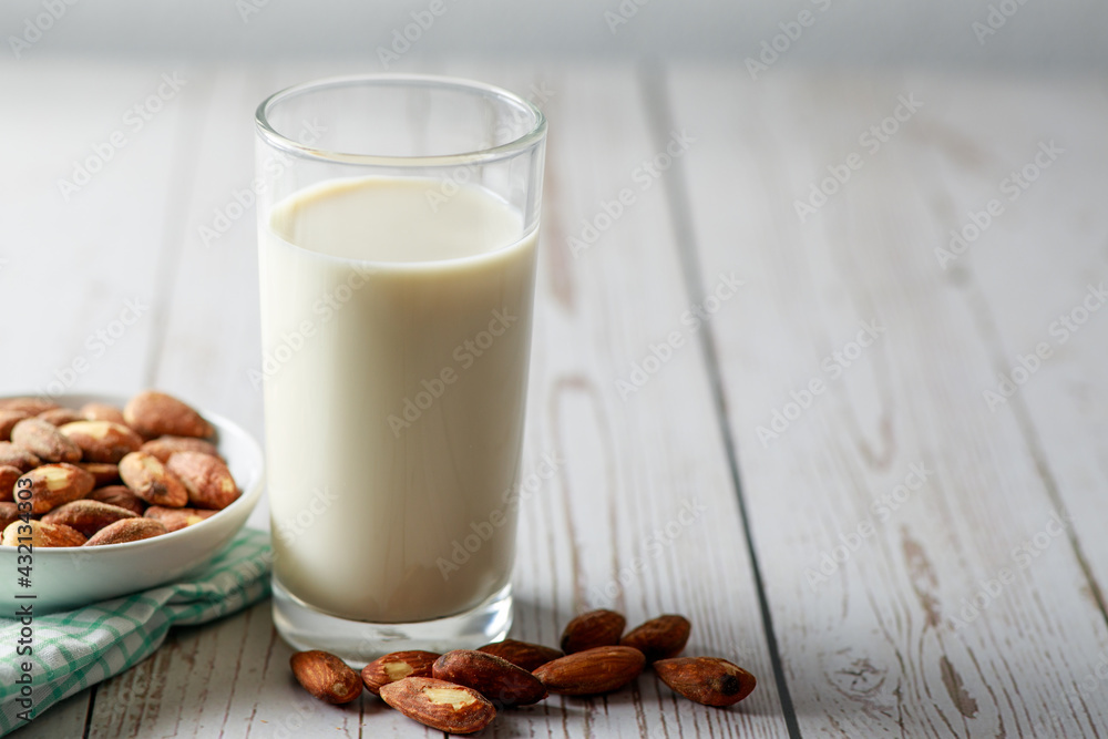 Almond milk in glass with kernel almonds on white wooden background. Healthy eating. Selective focus