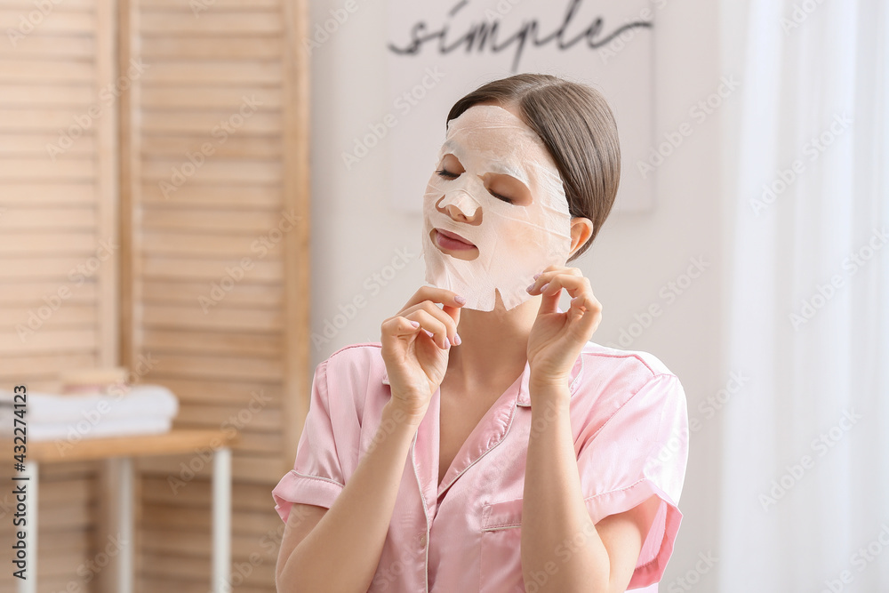 Beautiful young woman with sheet facial mask in bathroom