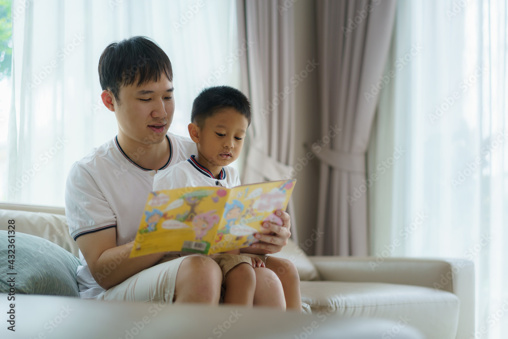 Asian father holds a book to teach his children to read on the sofa in the living room, fathers inte