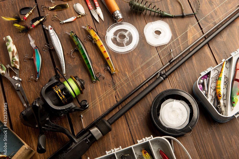 Fishing tackle - fishing spinning rod, hooks and lures on wooden background. Active hobby recreation