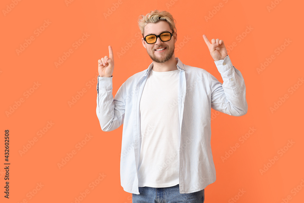 Young man with stylish sunglasses pointing at something on color background