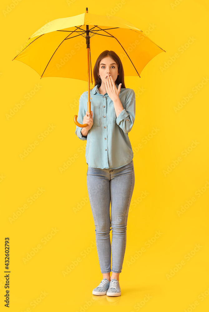 Surprised young woman with umbrella on color background