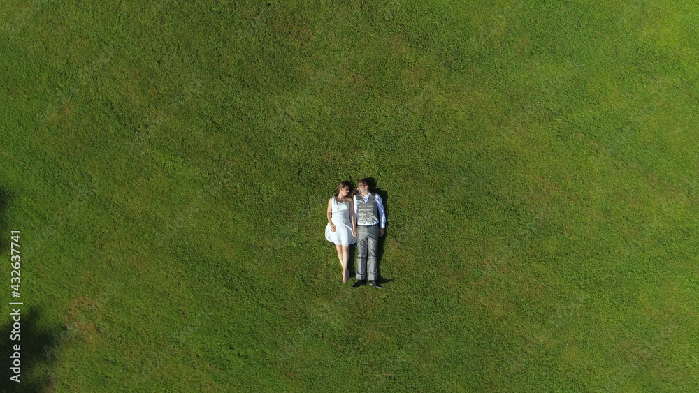 AERIAL TOP DOWN: Young loving parents to be lying down on grass on sunlit day