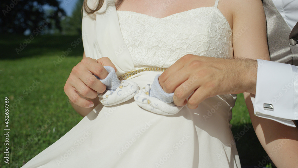 CLOSE UP: Pregnant couple holding a pair of tiny baby shoes over pregnant belly