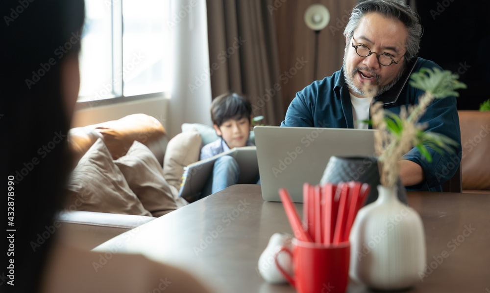 Asian middle aged man sitting at home working with family at home. Work from home concept