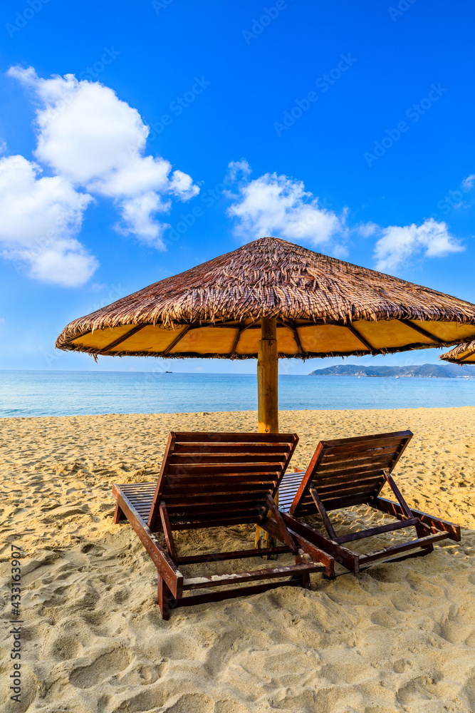 Wooden sun bed and umbrella on tropical beach in summer day.