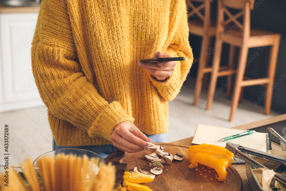 Young woman taking photo of sliced mushrooms in kitchen