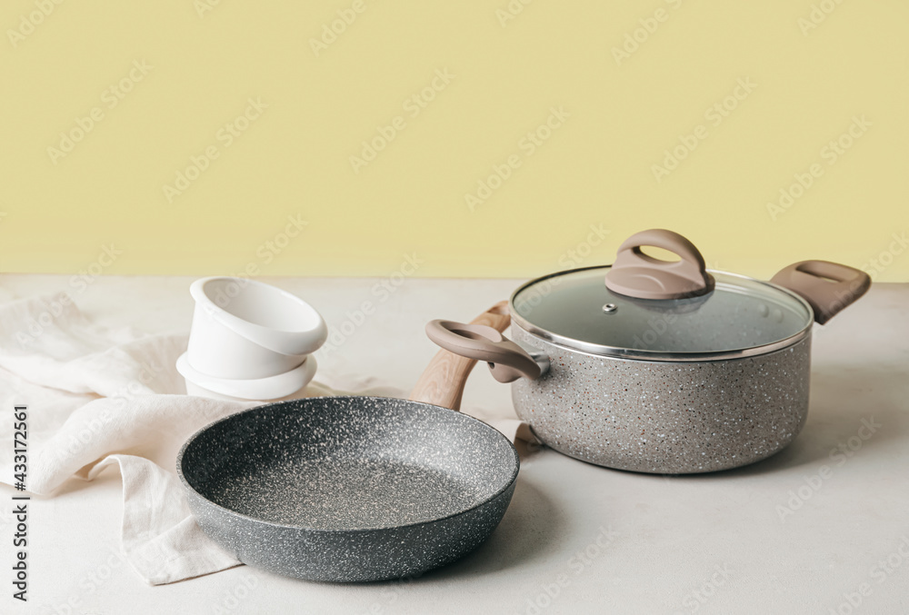 Frying pan and cooking pot on color background