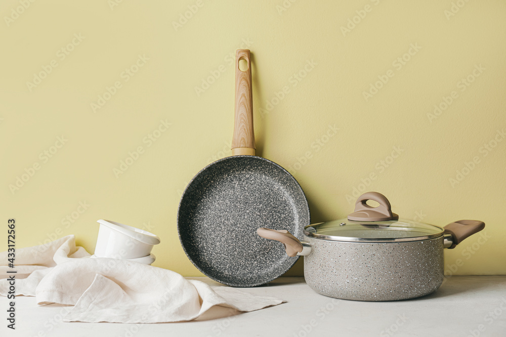 Frying pan and cooking pot on color background