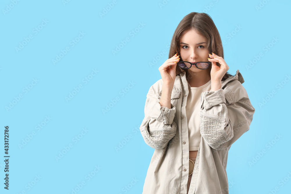 Young woman wearing eyeglasses on color background