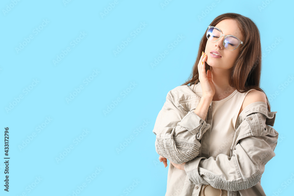 Young woman wearing eyeglasses on color background