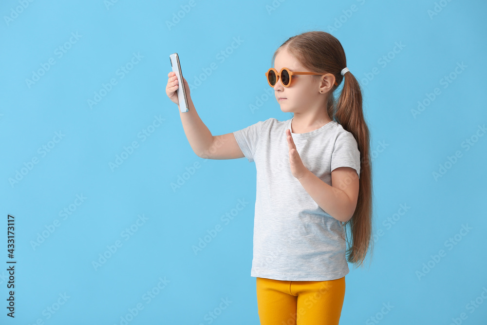 Cute little girl taking selfie on color background