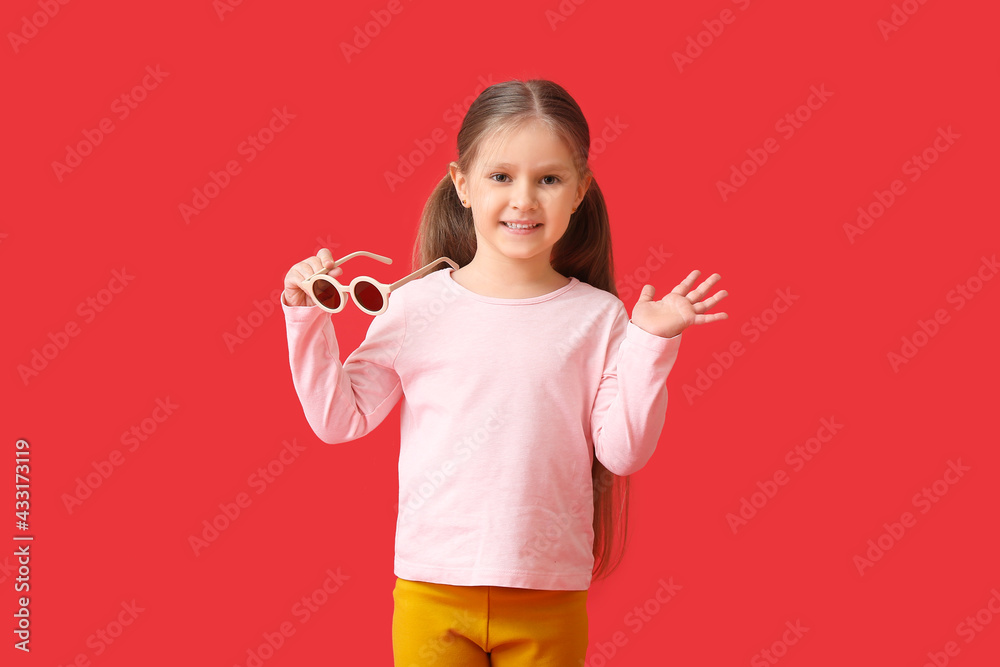 Cute little girl with stylish sunglasses on color background