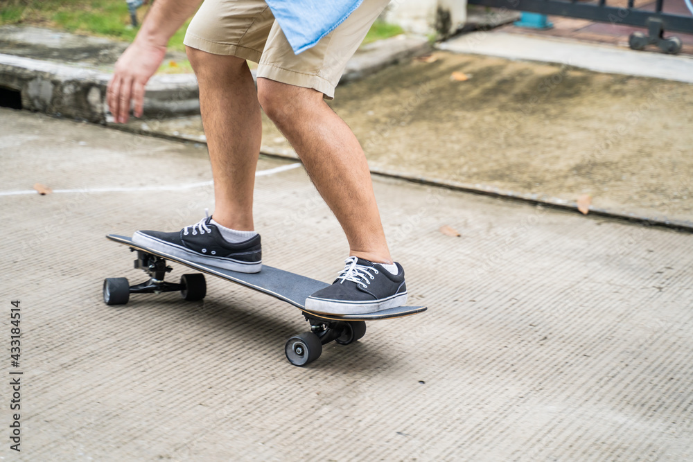 Close-up shot of Asian man surfing skate board on street for exercise.