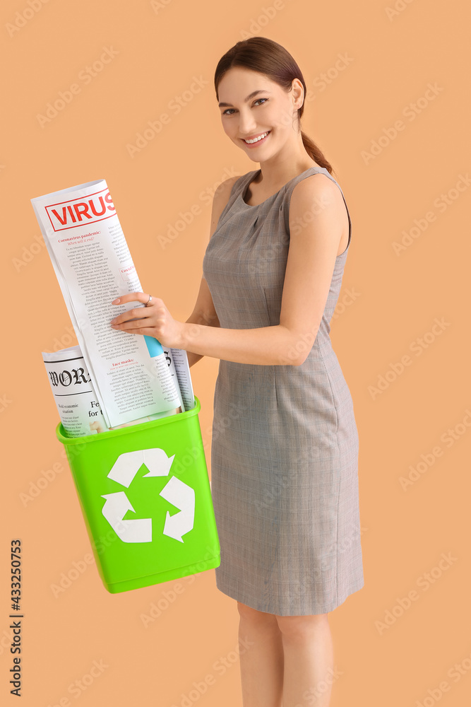 Young businesswoman with newspapers in trash bin with recycling symbol on color background