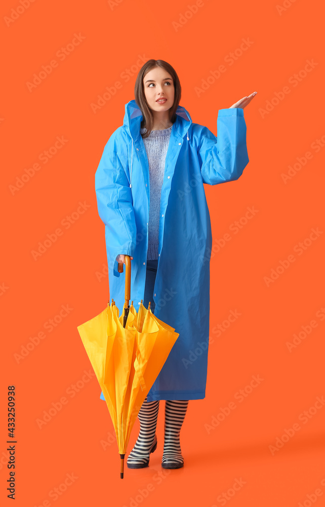 Stylish young woman in raincoat and with umbrella on color background