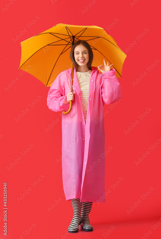 Stylish young woman in raincoat and with umbrella on color background