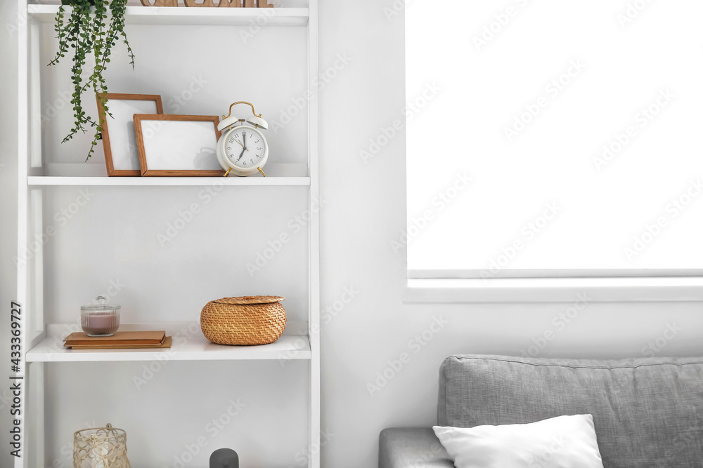 Modern shelf with alarm clock and decor near white wall