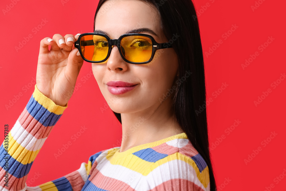 Beautiful young woman wearing stylish sunglasses on color background