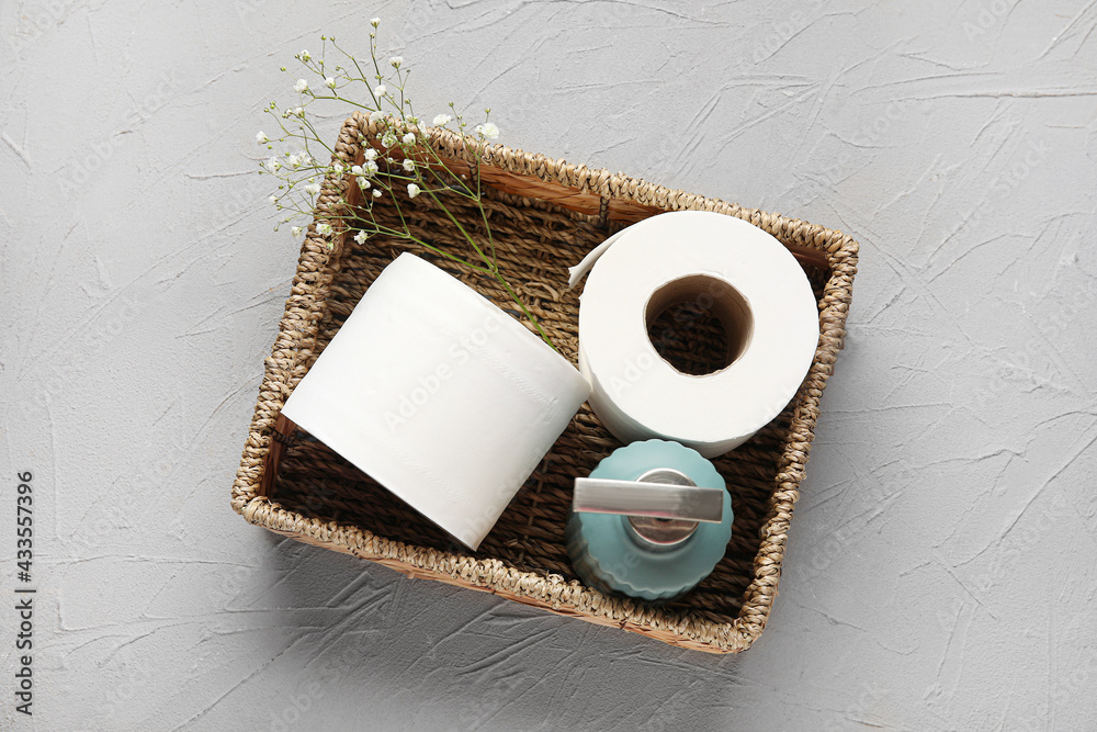 Basket with rolls of toilet paper, bottle of cosmetic product and flowers on dark background