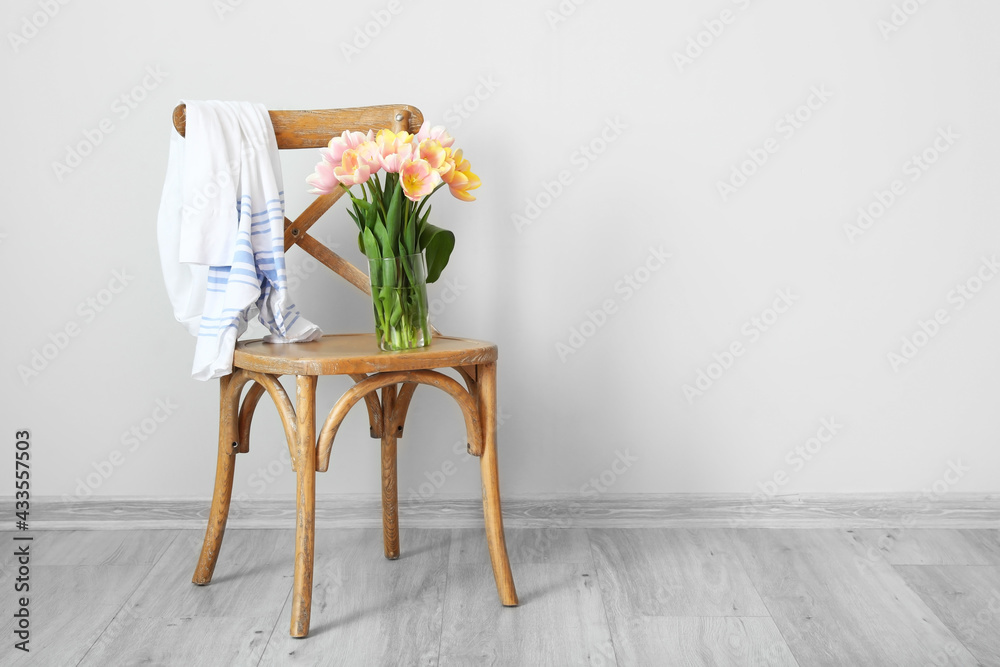 Bouquet of beautiful tulip flowers on chair near white wall in room