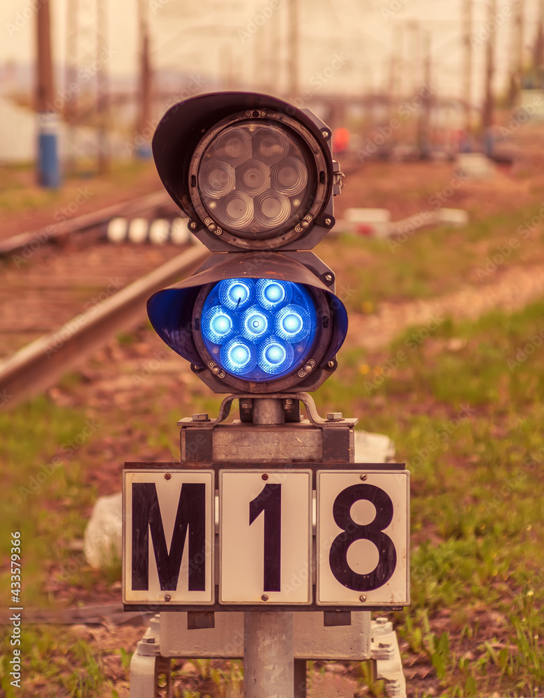 Small railway traffic light with blue-light signal standing near the railway tracks