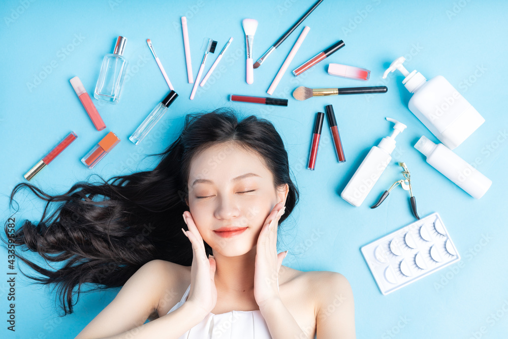 Asian woman lying on blue background with makeup around