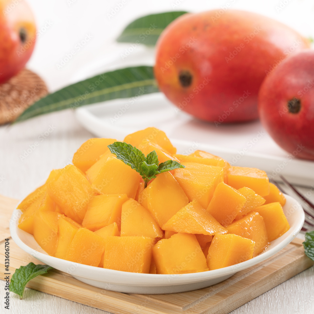 Diced fresh mango fruit on a white plate with leaves.