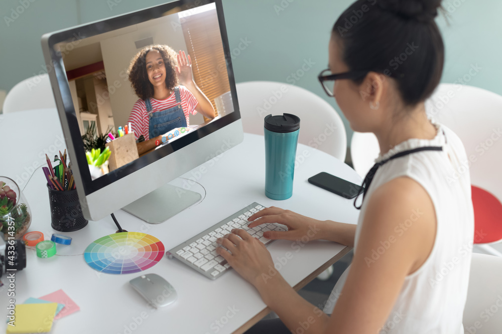 Asian businesswoman sitting at desk using computer having video call with female colleague