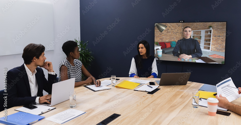 Diverse group of business colleagues having video call with businesswoman on screen in meeting room