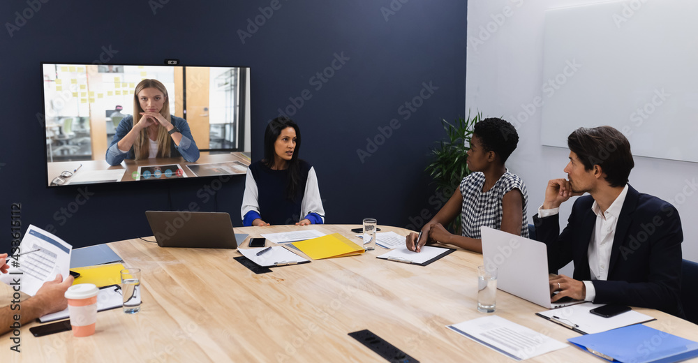 Diverse group of business colleagues having video call with businesswoman on screen in meeting room