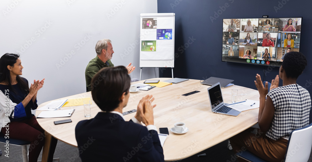 Diverse group of business colleagues having video call with coworkers on screen in meeting room