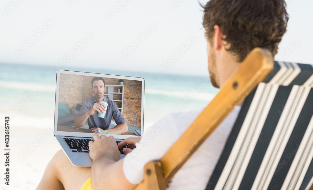 Caucasian man relaxing on beach having video call using laptop