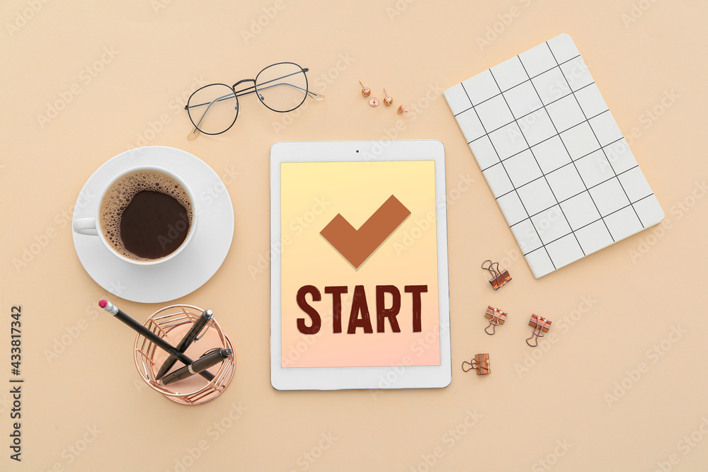 Text START on screen of tablet computer, stationery and cup of coffee on color background